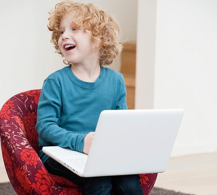 Elementary student sitting in a chair with his laptop - Connections Academy